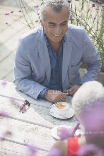 Coppia anziana parlando e bevendo caffè al tavolo soleggiato patio — Foto stock