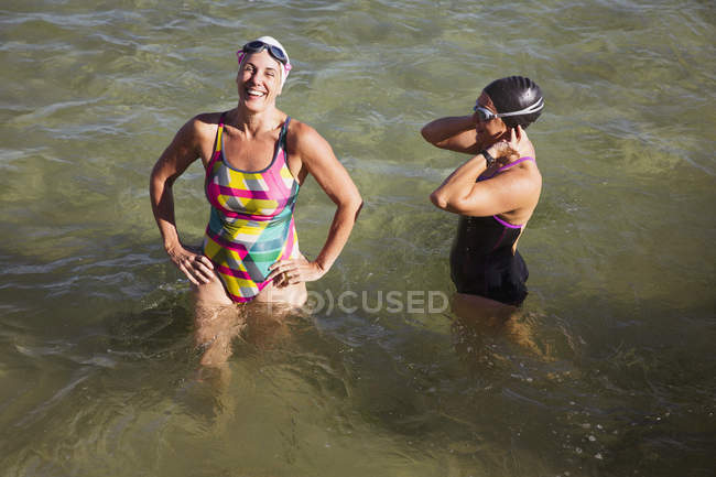Riendo mujeres nadadoras de aguas abiertas vadeando en el océano soleado - foto de stock