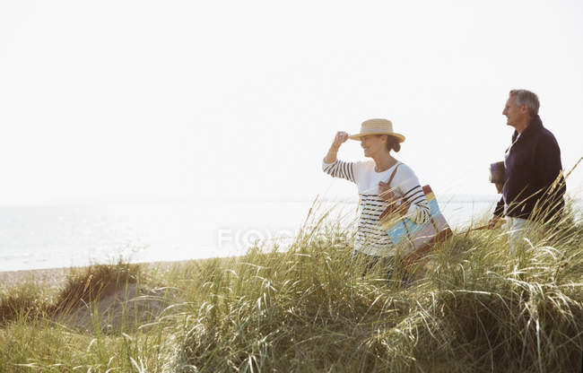 Casal maduro andando na grama ensolarada praia — Fotografia de Stock