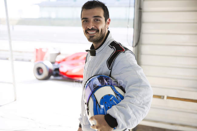 Retrato seguro de fórmula masculina un conductor de coche de carreras que sostiene el casco en el garaje de reparación - foto de stock