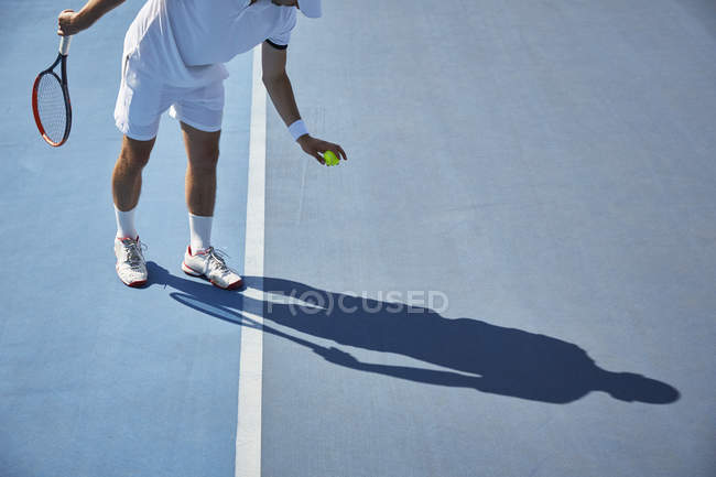 Young male tennis player playing tennis, bouncing tennis ball on sunny blue tennis court — Stock Photo
