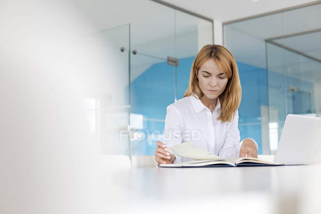 Mujer de negocios enfocada revisando el papeleo en el portátil en la sala de conferencias - foto de stock