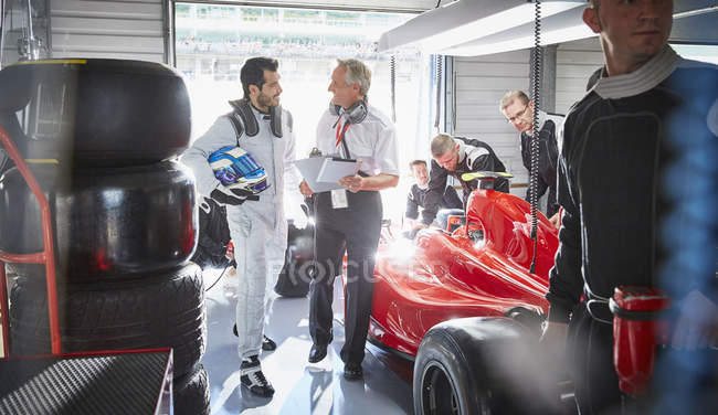 Manager und Formel-1-Rennfahrer im Gespräch in Reparaturwerkstatt — Stockfoto