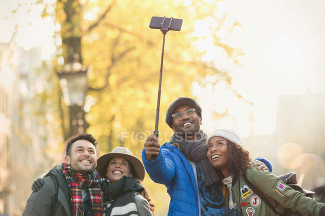 Sorrindo jovens amigos casal tomando selfie com vara selfie na rua de outono — Fotografia de Stock