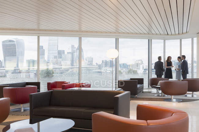 Geschäftsleute unterhalten sich am Fenster in der städtischen Hochhaus-Büro-Lounge mit Blick auf die Stadt — Stockfoto