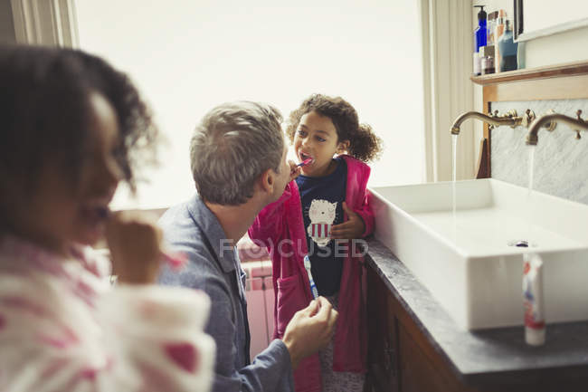 Multi-étnico padre viendo hija cepillarse los dientes en el lavabo del baño - foto de stock