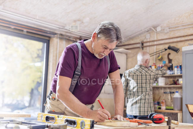 Tischler misst und markiert Holzplanke auf Werkbank in Werkstatt — Stockfoto