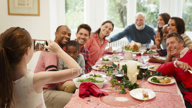 Menina com câmera telefone fotografar família multi-étnica na mesa de jantar de Natal — Fotografia de Stock
