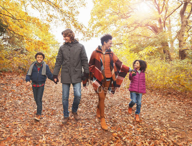 Молодая семья держится за руки и ходит по осенним лесам — стоковое фото