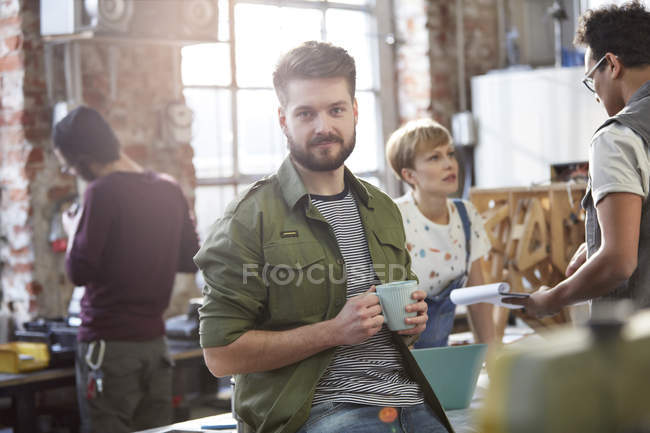 Portrait confident young male designer drinking coffee in workshop — Stock Photo