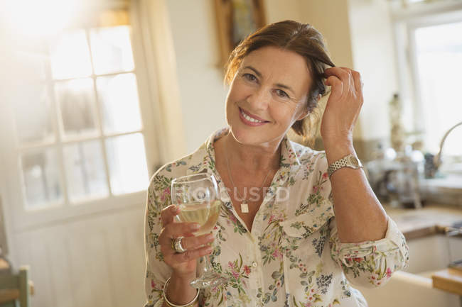 Portrait smiling mature woman drinking white wine in kitchen — Stock Photo