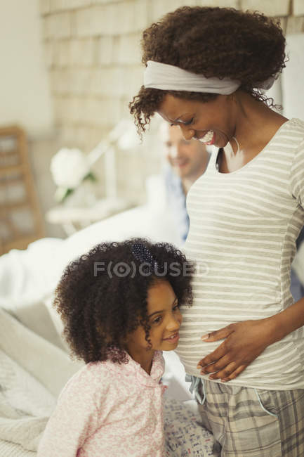 Curious daughter listening to pregnant mother?s stomach — Stock Photo