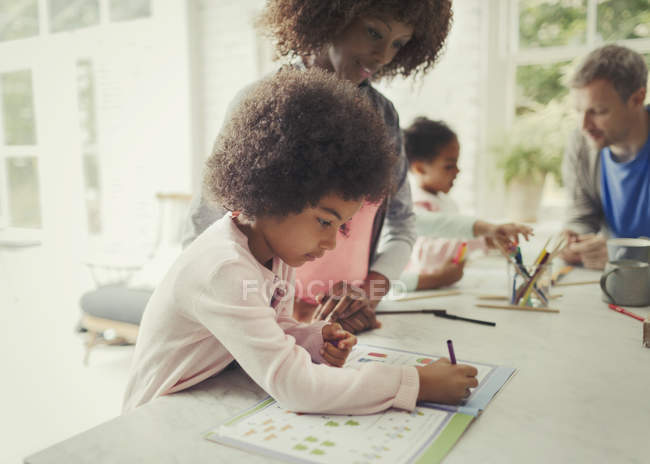 Mãe assistindo filha colorir em livro de atividades na cozinha — Fotografia de Stock