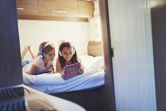Sisters with headphones sharing digital tablet, watching video inside motor home — Stock Photo