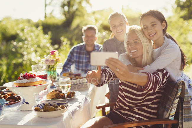 Mãe e filhas tomando selfie com telefone da câmera na mesa do pátio da festa do jardim — Fotografia de Stock