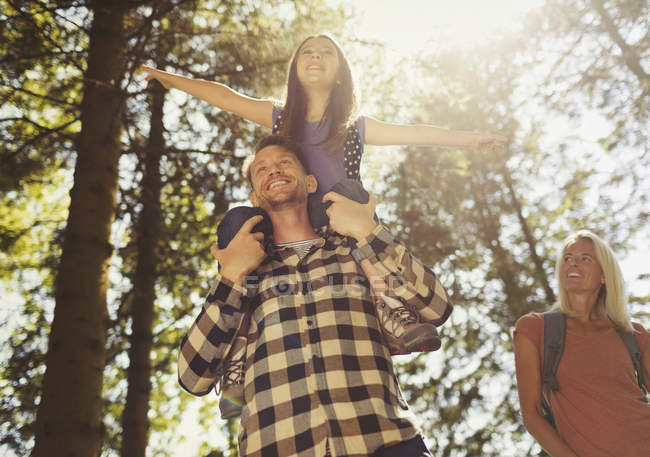 Отец носит дочь на плечах, путешествует в солнечных лесах — стоковое фото