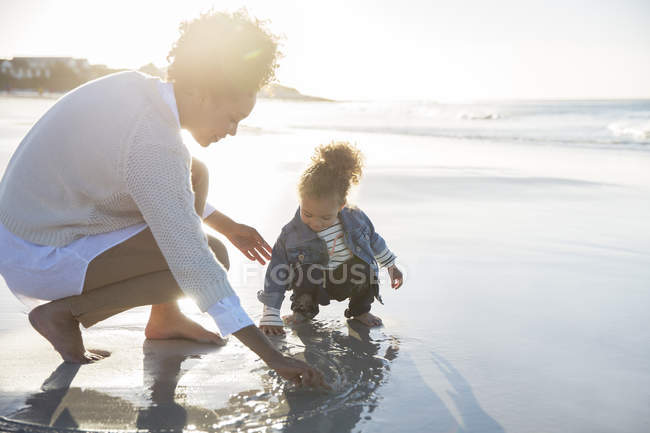 Madre e hija dibujando sobre arena mojada en la playa - foto de stock