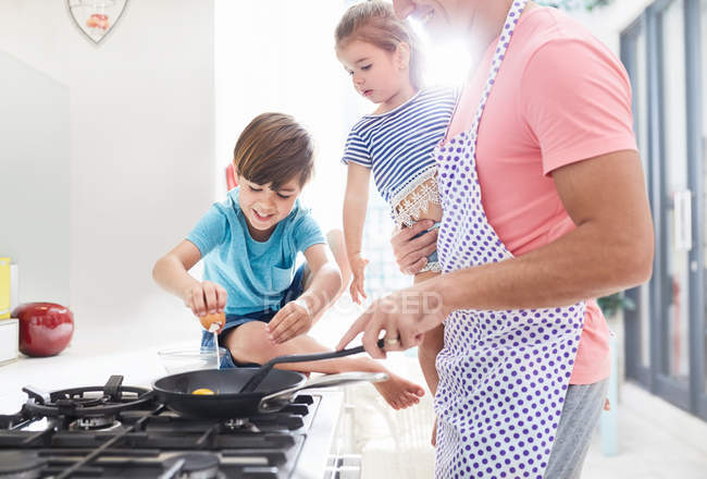 Padre cocinando el desayuno en la estufa con hija e hijo - foto de stock
