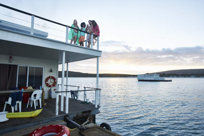 Jóvenes amigos adultos pasando el rato en la cubierta de la casa flotante de verano en el océano - foto de stock