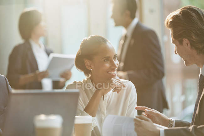 Улыбающиеся бизнесмены обсуждают бумажную работу на встрече — стоковое фото