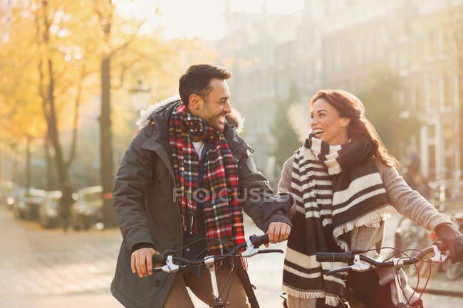 Smiling young couple in warm clothing bike riding on urban autumn street — Stock Photo
