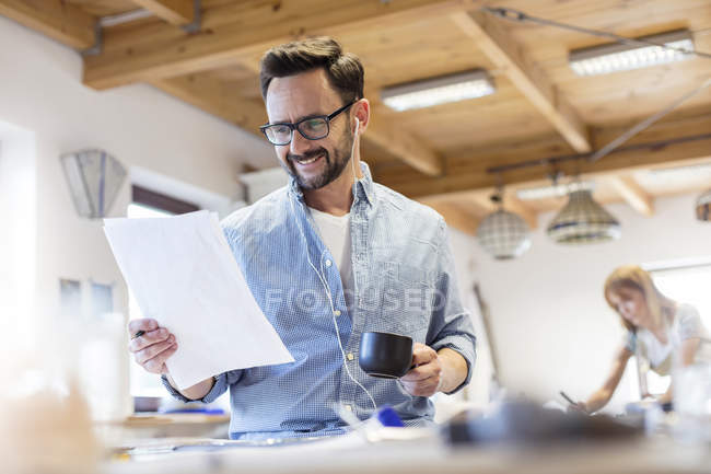 Smiling artist reviewing drawings in studio and listening to music with earbuds — Stock Photo
