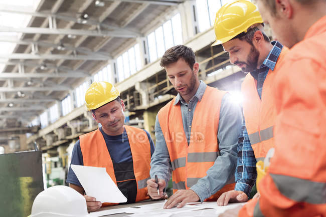 Steel workers and engineers meeting reviewing blueprints in factory — Stock Photo