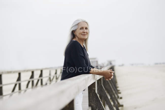 Портрет уверенной пожилой женщины, опирающейся на перила на пляже — стоковое фото