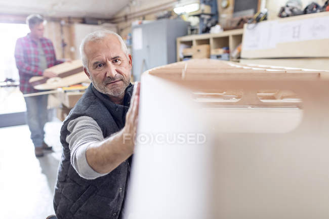 Homme charpentier examinant, touchant bateau en bois dans l'atelier — Photo de stock