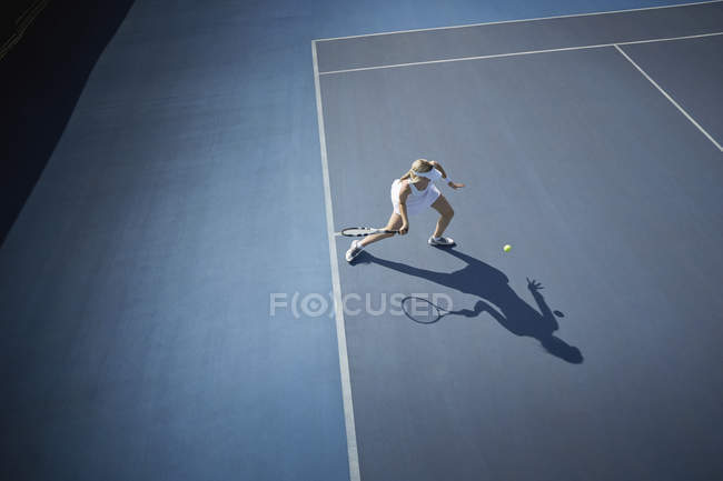 Vue aérienne jeune joueuse de tennis jouant au tennis, frappant la balle sur un court de tennis bleu ensoleillé — Photo de stock