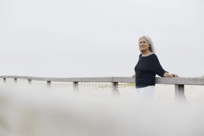 Confident senior woman leaning on beach boardwalk railing — Stock Photo