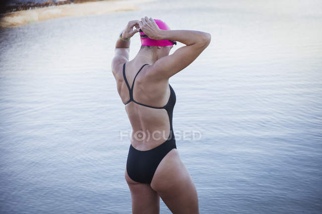 Female open water swimmer adjusting swimming goggles at ocean — Stock Photo