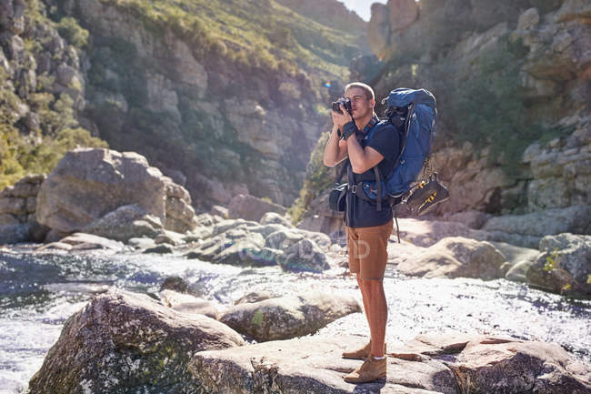 Jovem com mochila caminhadas, fotografando com câmera em rochas ensolaradas — Fotografia de Stock