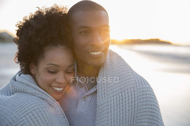 Portrait of couple wrapped in blanket on beach — Stock Photo
