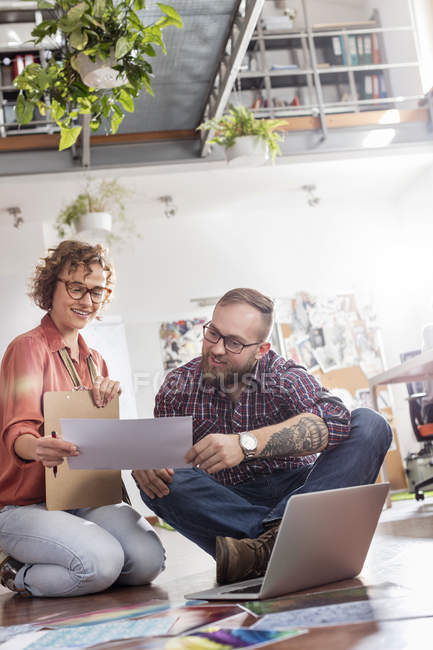 Design professionals discussing proofs at laptop on office floor — Stock Photo