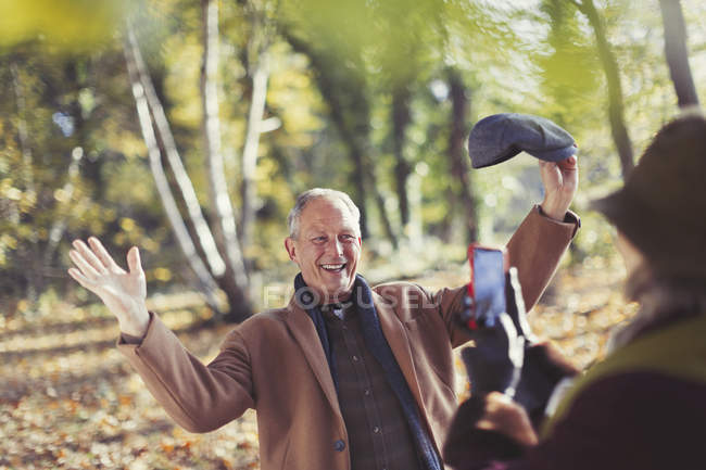 Senior man posing for wife with camera phone in autumn park — Stock Photo