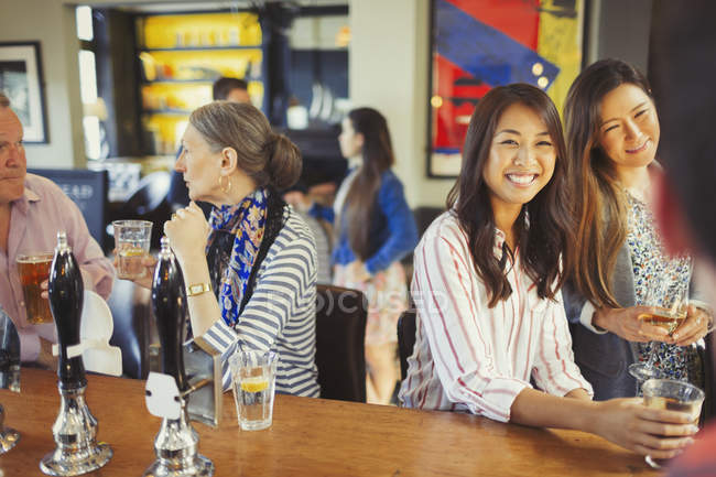 Women smiling at bartender and drinking at bar — Stock Photo