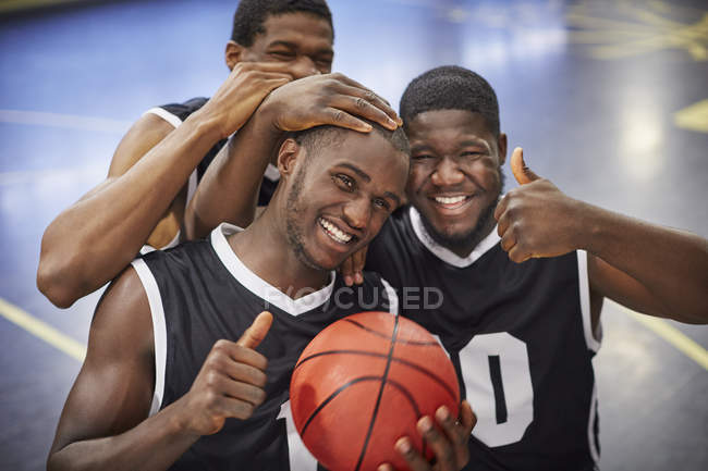 Retrato sonriente, confiado equipo joven jugador de baloncesto masculino celebrando, señalando pulgares hacia arriba - foto de stock
