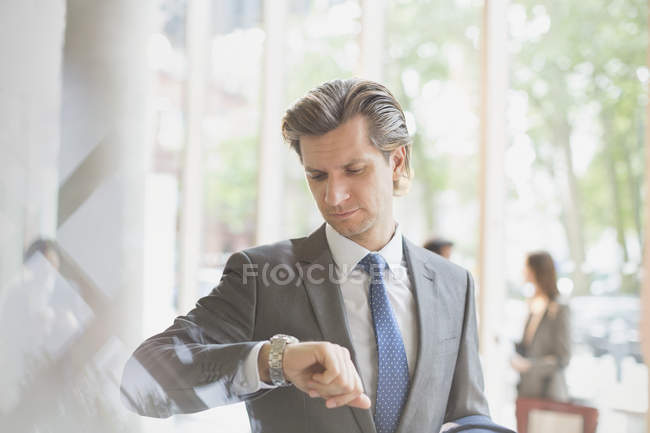 Empresário verificando o tempo no relógio de pulso no lobby do escritório — Fotografia de Stock