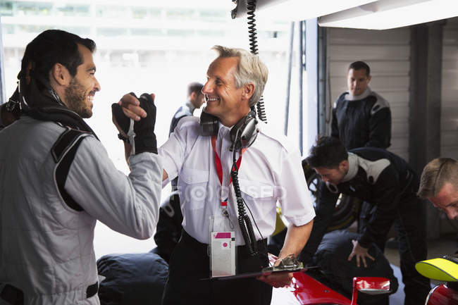 Manager and formula one driver celebrating, handshaking in repair garage — Stock Photo