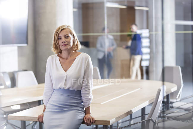 Porträt selbstbewusste Geschäftsfrau lehnt am Konferenzzimmertisch — Stockfoto
