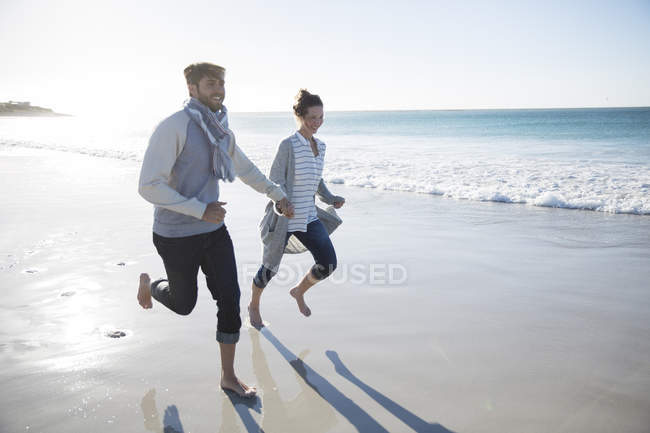 Jovem casal de mãos dadas e correndo na praia — Fotografia de Stock