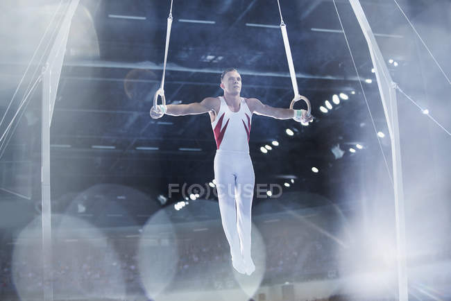 Male gymnast performing on gymnastics rings in arena — Stock Photo