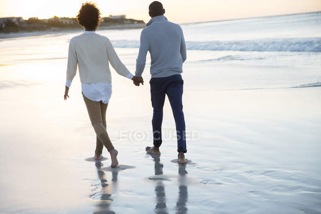 Pareja joven cogida de la mano y caminando en la playa - foto de stock