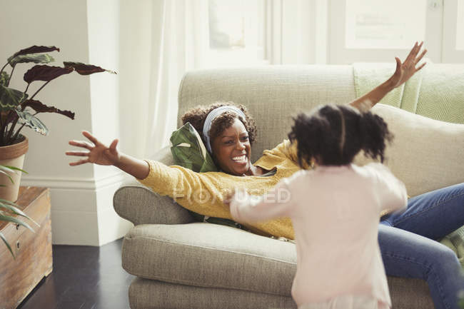Mère enthousiaste sur le canapé saluant fille en cours d'exécution — Photo de stock