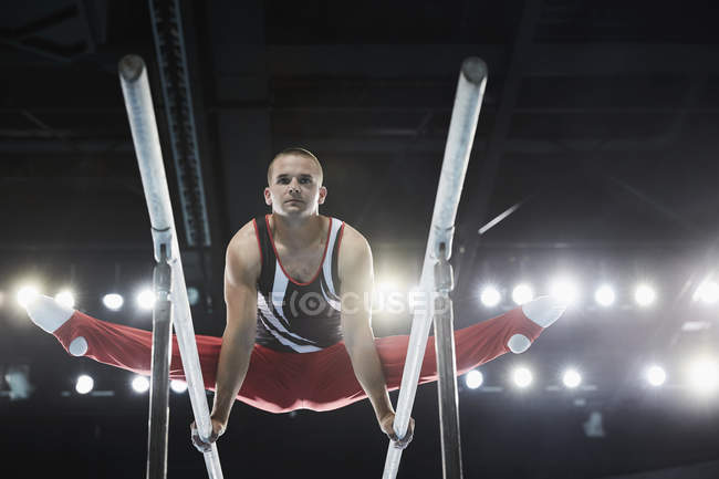 Male gymnast performing splits on parallel bars — Stock Photo