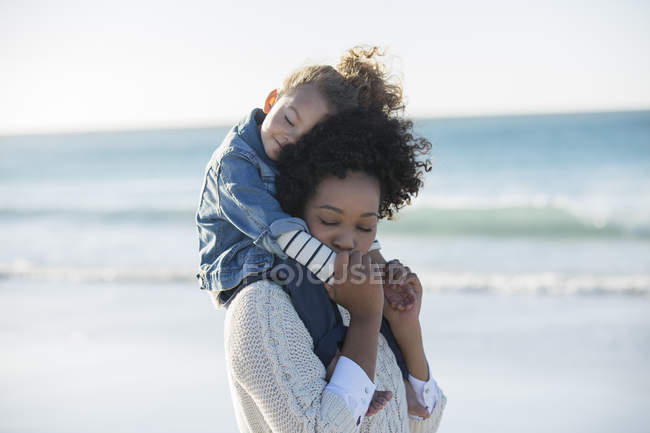 Мати носить дочку на плечах на пляжі — стокове фото