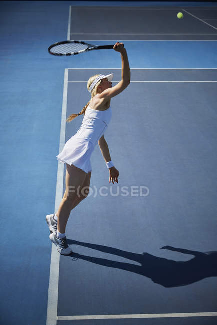 Young female tennis player playing tennis, reaching with tennis racket on sunny blue tennis court — Stock Photo