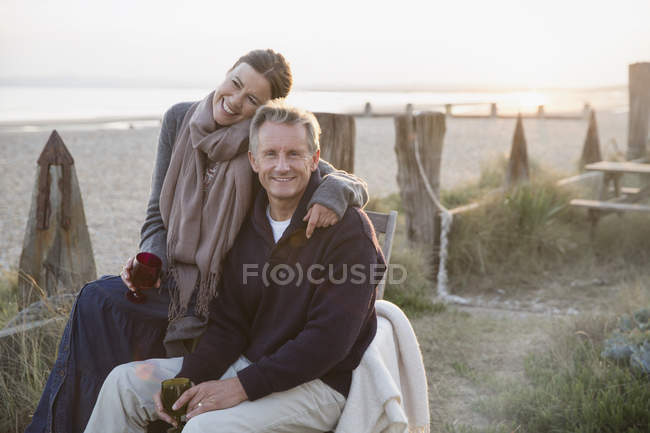 Retrato cariñoso pareja madura bebiendo vino en la playa puesta del sol - foto de stock