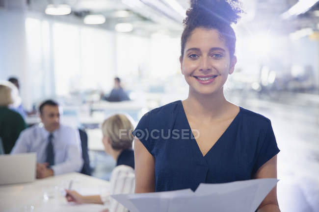 Porträt lächelnde, selbstbewusste junge Geschäftsfrau mit Papierkram im Büro — Stockfoto